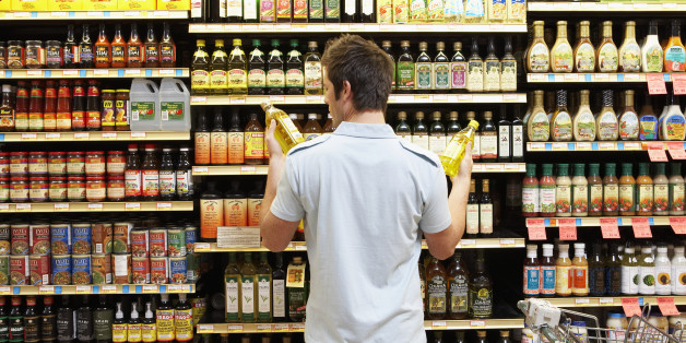 Young man in supermarket comparing bottles of oil, rear view, close-up